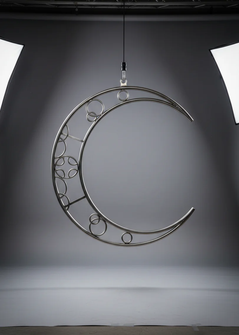 Professional volumetric aerial moon lyra made of polished stainless steel, featuring a decorative internal truss design, hanging in a bright white photo studio.